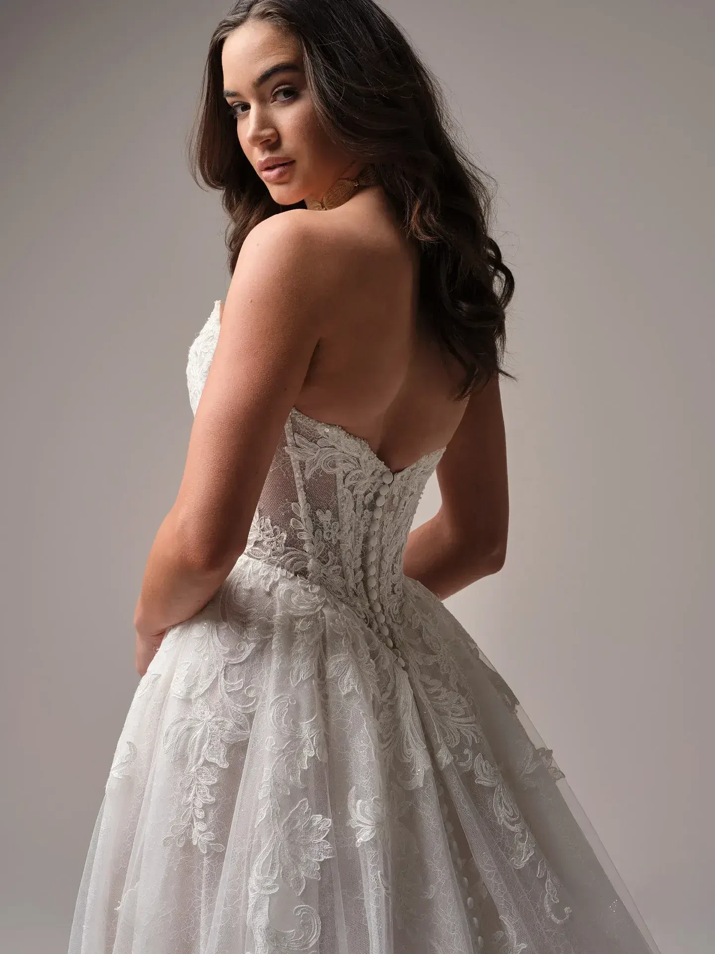 Model is wearing a soft satin sheath dress with asymmetrical sweetheart neckline, unlined bodice, and Chantilly lace with glitter tulle overlay.