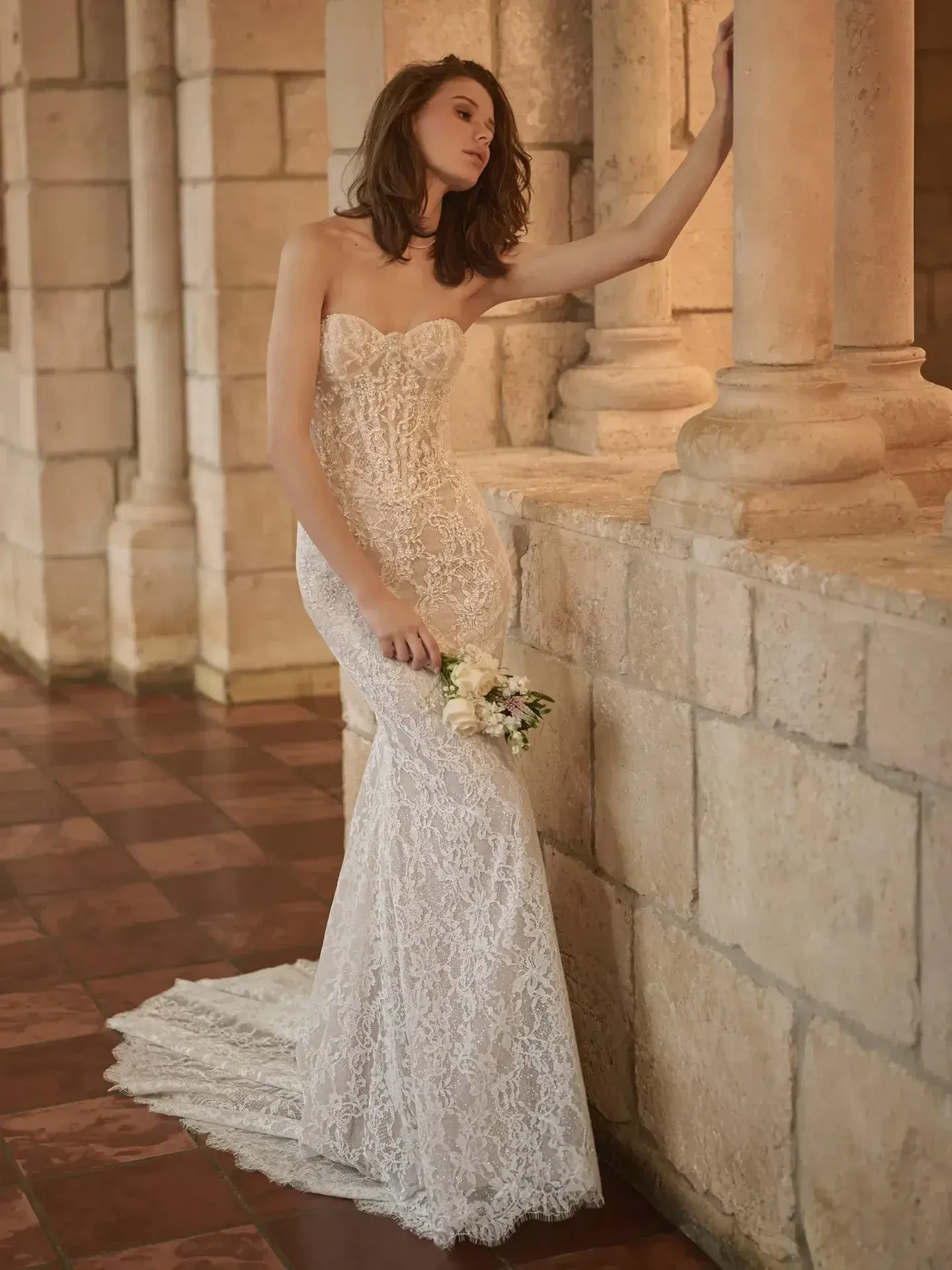 Model is wearing a mermaid gown featuring a sexy illusion lace back and intricate lace accents along a fitted silhouette.