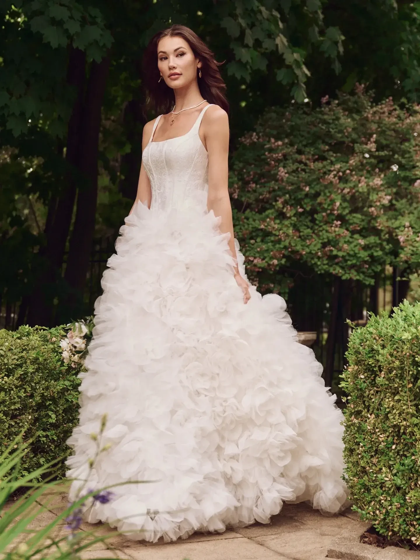 Model is wearing a ruffled jacquard wedding dress with a square neckline and full skirt