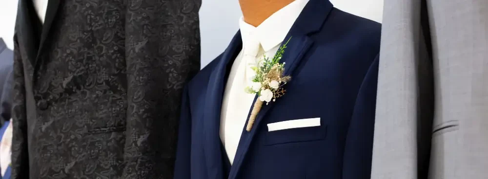 A tailored suit with a boutonniere, displayed alongside two other suits.