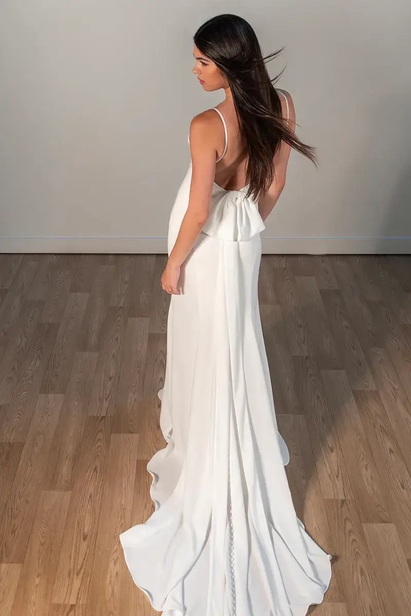 Model is wearing a column bridal gown with a scoop neckline and low back