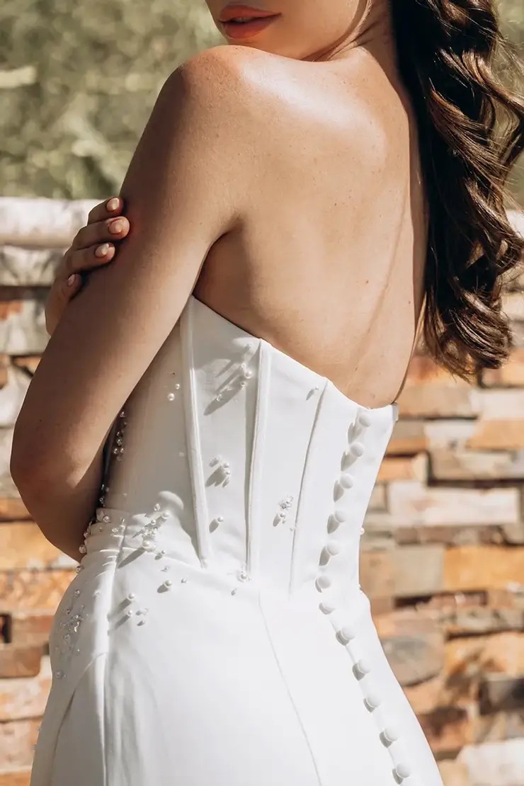 Model is wearing a column wedding dress with a strapless bodice and 3D floral accents