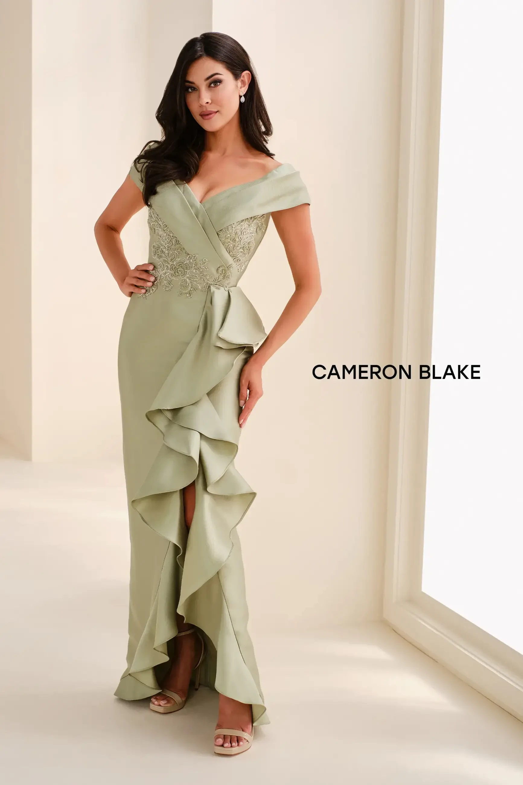 A woman wearing a light green evening gown with ruffles, posing confidently.