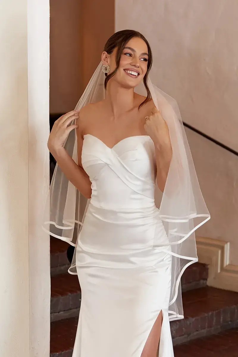 Model is wearing a column wedding dress that’s strapless and sleek