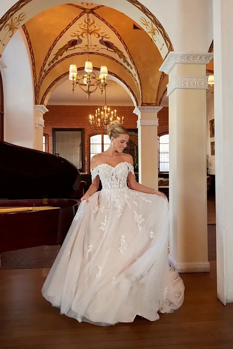 Model is wearing an a-line floral lace bridal gown with a sweetheart neckline and off the shoulder lace straps 