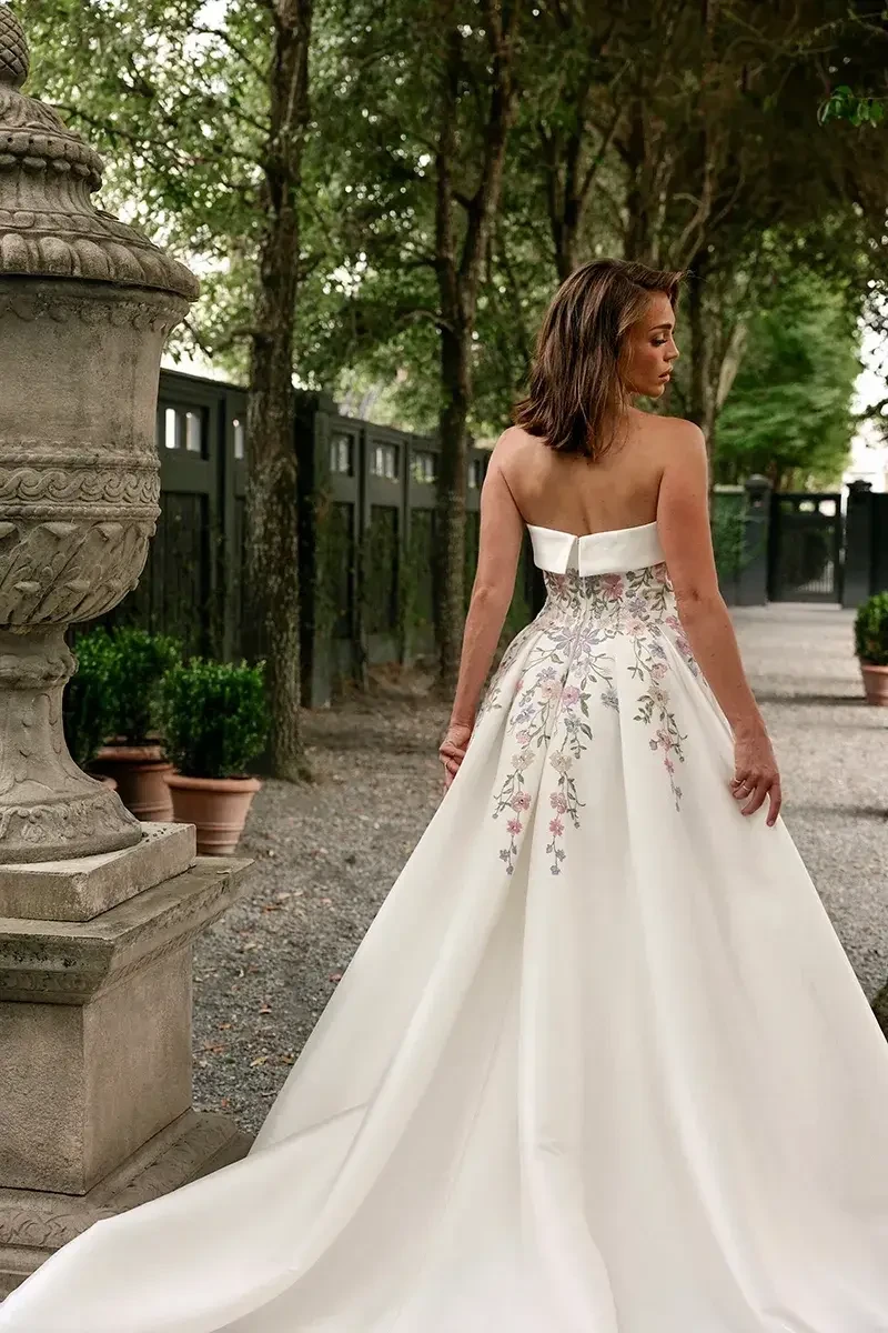 Model is wearing a strapless mikado ball gown with pastel floral embroidery