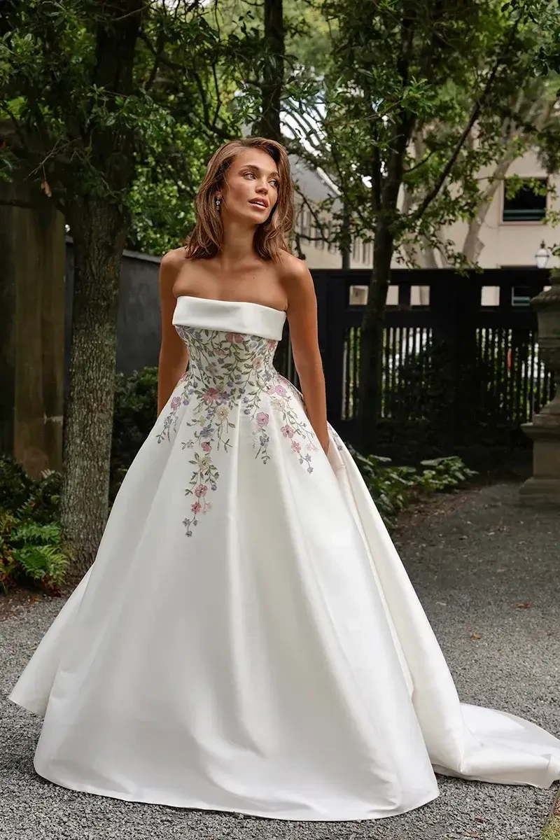 Model is wearing a strapless mikado ball gown with pastel floral embroidery