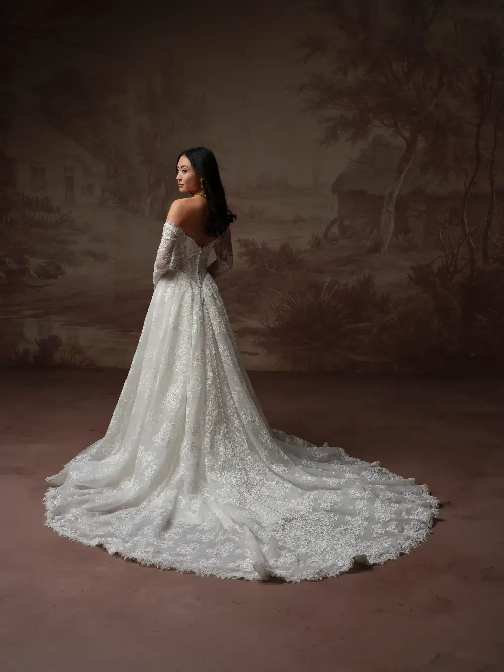A woman in an elegant white wedding dress, standing with her back to the camera, against a vintage-style backdrop.