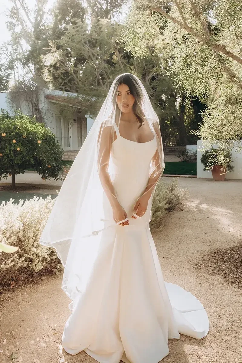 Model is wearing a fit-and-flare wedding dress with a structured corset bodice, wide straps, and a trumpet skirt.